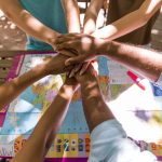 773630 - Fundación Trébol Educación | CR Diario Group of people placing hands together over a world map on a table, symbolizing teamwork in planning travel or a project.