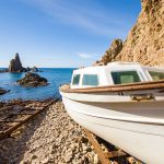 Cabo de Gata in Almeria Spain | CR Diario White boat resting on a rocky pebbled shore with blue sea behind it and clear sky.