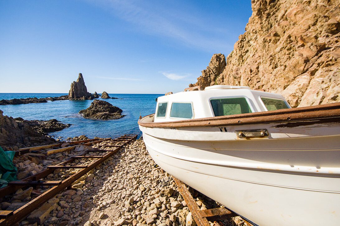 Cabo de Gata in Almeria Spain | CR Diario White boat resting on a rocky pebbled shore with blue sea behind it and clear sky.