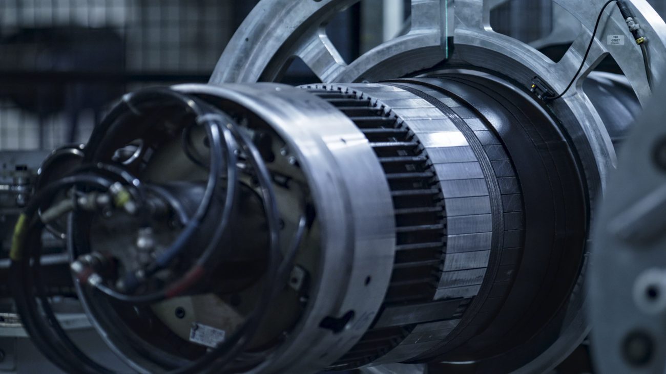 Close-up of a large industrial turbine/jet engine shaft with metallic rings and wiring in a maintenance setting.