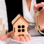 780370 - Finques Sant Pol | CR Diario Person in business attire holds a wooden house model and a set of keys, symbolizing real estate or homeownership.