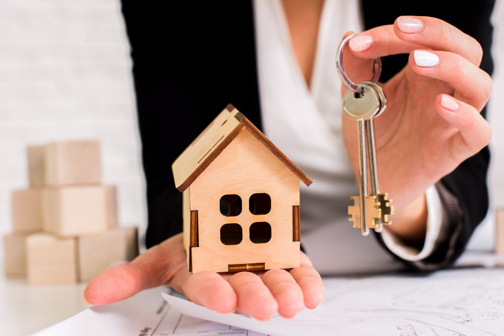 780370 - Finques Sant Pol | CR Diario Person in business attire holds a wooden house model and a set of keys, symbolizing real estate or homeownership.
