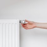 Person adjusting a white radiator valve knob with a fingertip, likely controlling heat output