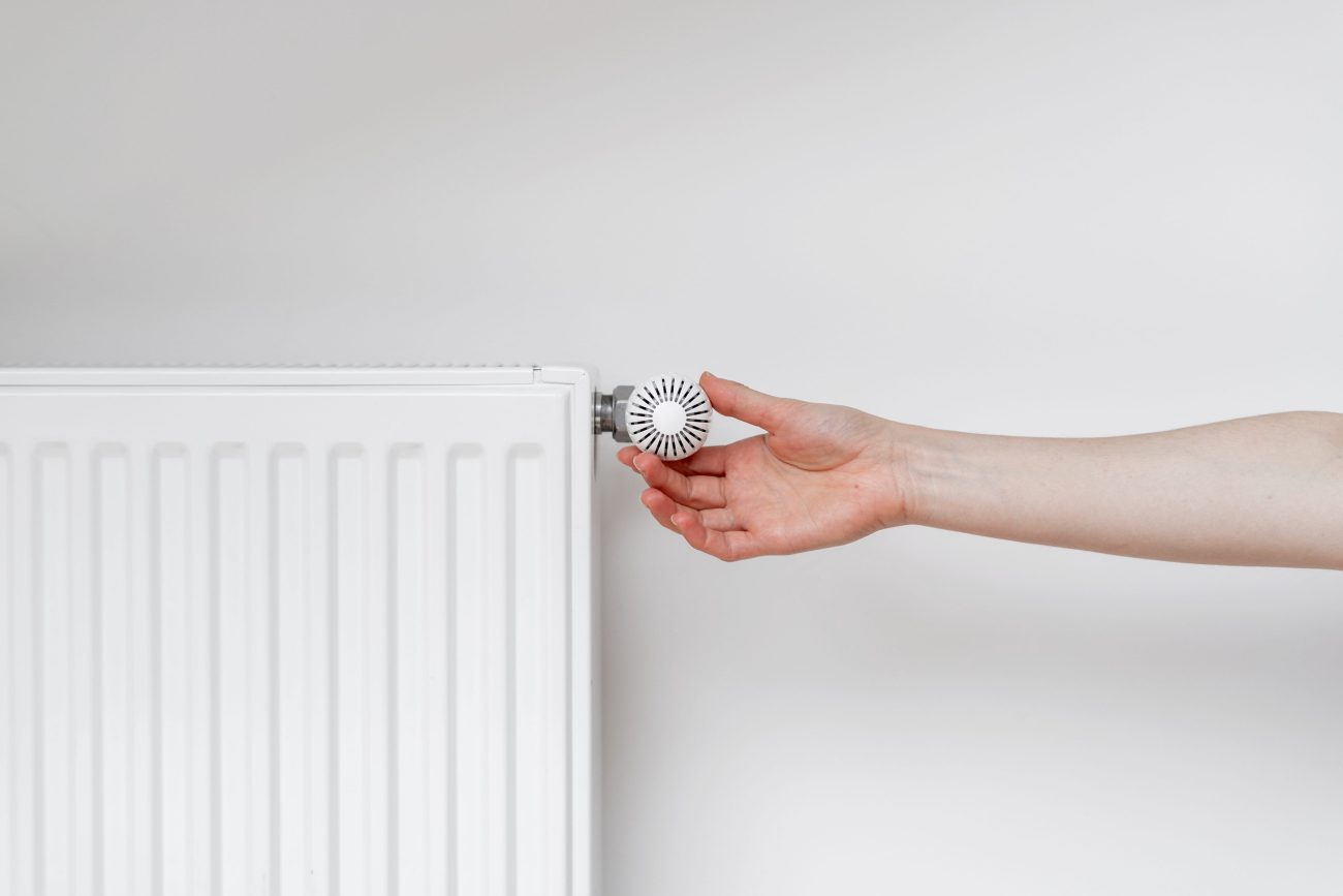 Person adjusting a white radiator valve knob with a fingertip, likely controlling heat output