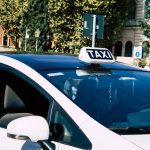 Digiman taxista - IP | CR Diario White taxi with a TAXI sign on its roof parked on a city street area.