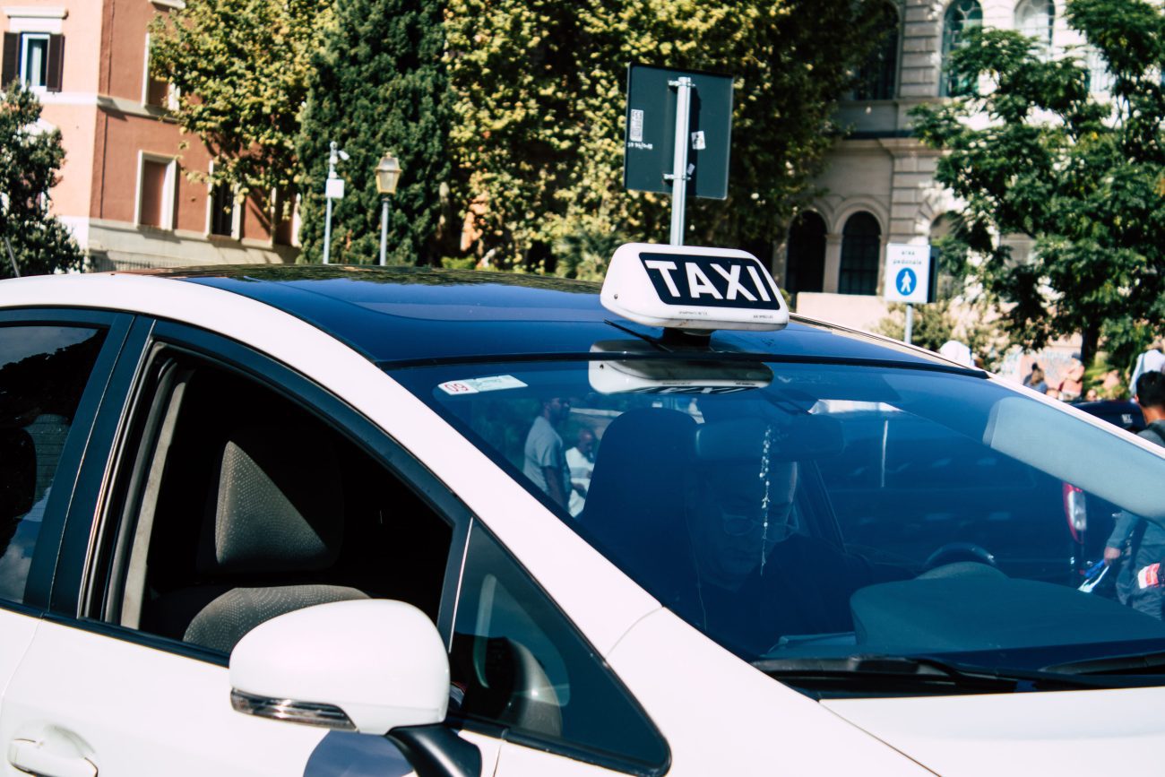 Digiman taxista - IP | CR Diario White taxi with a TAXI sign on its roof parked on a city street area.