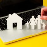 785090 - Abogados Fincas Madrid | CR Diario Paper cutouts of a house and a family placed on a laptop keyboard, with a hand arranging the figures, symbolizing online housing or family planning